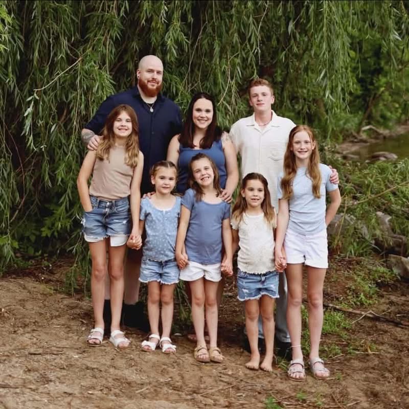 Erica Lee with her husband and their six children, standing together under a willow tree